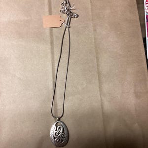 Puede incluir: Un collar de plata con un colgante con un dise&ntilde;o de espiral. El colgante tiene forma ovalada y una cadena delicada.