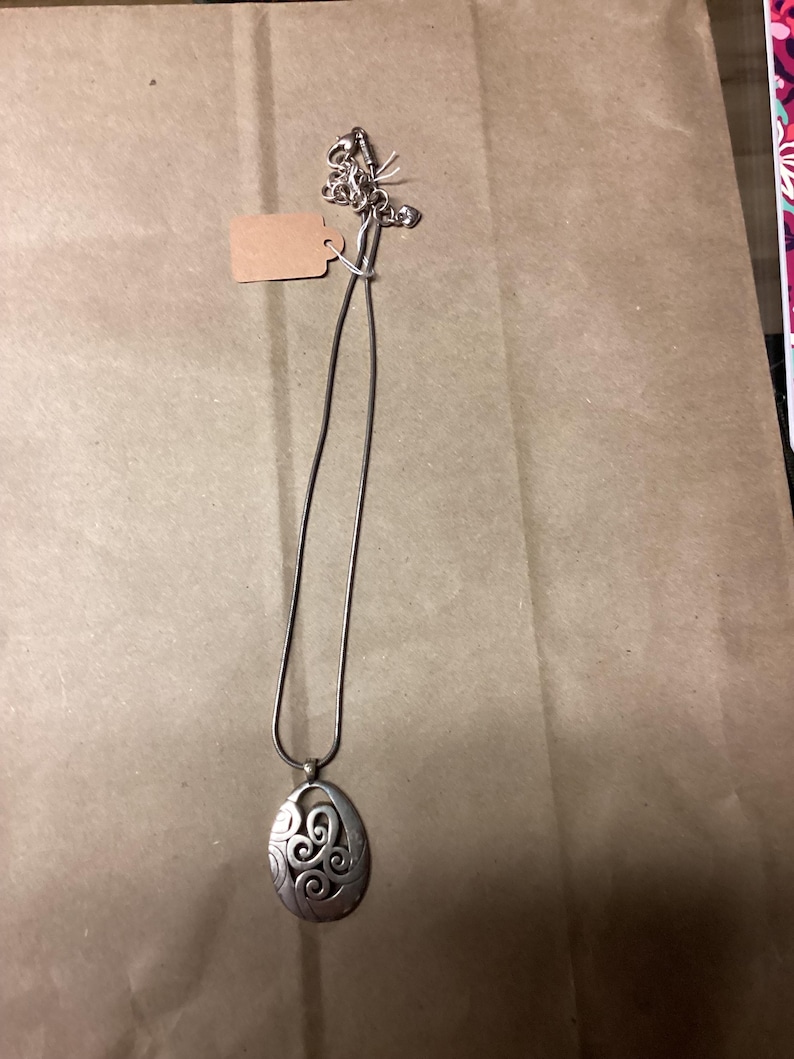 Puede incluir: Un collar de plata con un colgante con un dise&ntilde;o de espiral. El colgante tiene forma ovalada y una cadena delicada.