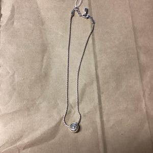 May include: A silver chain necklace with a round gold pendant. The pendant has a detailed design.