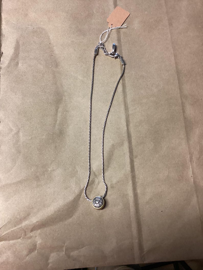 May include: A silver chain necklace with a round gold pendant. The pendant has a detailed design.