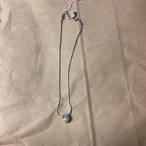 May include: A silver chain necklace with a round pendant featuring a gold-toned design.