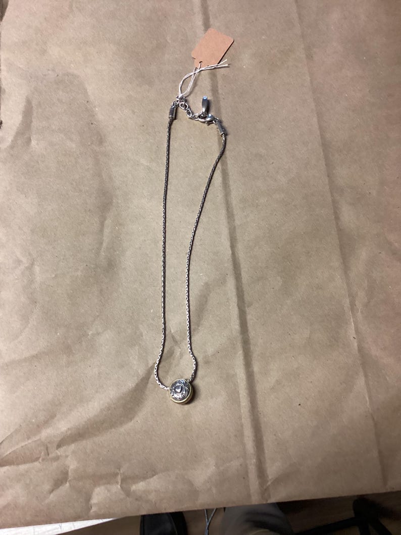 May include: A silver chain necklace with a round pendant featuring a gold-toned design.