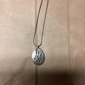 Puede incluir: Un collar de plata con un colgante con un dise&ntilde;o de espiral.