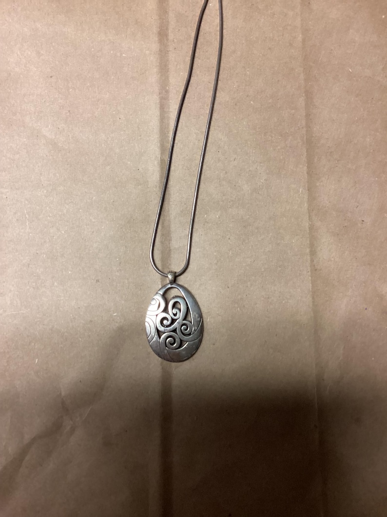 Puede incluir: Un collar de plata con un colgante con un dise&ntilde;o de espiral.