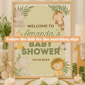May include: A framed baby shower sign with a light wood frame. The sign features jungle animal illustrations and the text "Welcome to Amanda's Baby Shower 05.02.2026". The sign also includes the text "Follow the link for the matching sign".