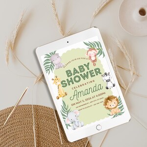 May include: A digital tablet shows a baby shower invitation. The invitation has a light green background with jungle animal illustrations, including a giraffe, zebra, lion, elephant, monkey, and hippo. Text reads "Baby Shower Celebrating Amanda".