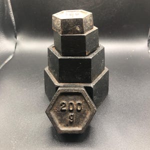 Könnte beinhalten: Ein Satz aus fünf schwarzen Gusseisengewichten, die in Pyramidenform gestapelt sind. Das unterste Gewicht ist ein sechseckiges Gewicht mit der Zahl "200" und dem Buchstaben "g" darauf.