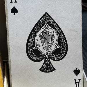 May include: A playing card from a deck, the Ace of Spades. The card features a large black spade symbol with an ornate design, including a harp and the words "TRADE MARK". The card also has the letter "A" and a smaller spade symbol.