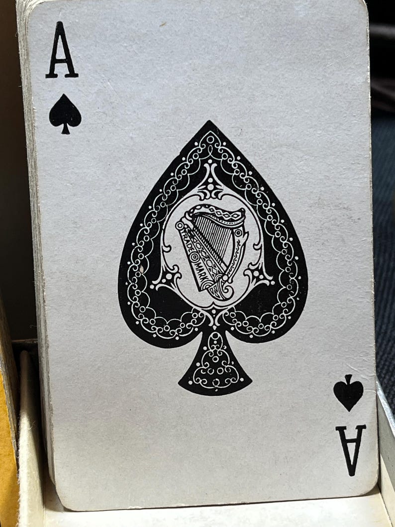 May include: A playing card from a deck, the Ace of Spades. The card features a large black spade symbol with an ornate design, including a harp and the words "TRADE MARK". The card also has the letter "A" and a smaller spade symbol.