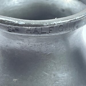 Puede incluir: Primer plano de una taza medidora vintage de metal gris. El texto "87 HALF GILL" est&aacute; grabado en el lateral. La taza tiene una superficie texturizada y un borde acampanado.