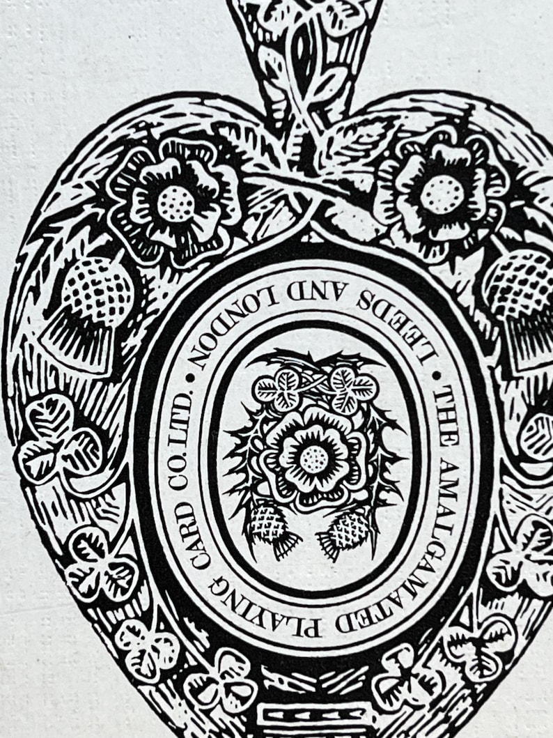 May include: Black and white illustration of a heart-shaped design with floral and leaf motifs. The text "THE AMALGAMATED PLAYING CARD CO. LTD. LEEDS AND LONDON" is visible within the design. The image has a vintage aesthetic.
