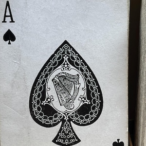 May include: Close-up of the Ace of Spades playing card. The card features a black spade symbol and the letter "A" in the upper left and lower right corners. The spade design includes a detailed harp illustration within a decorative border.