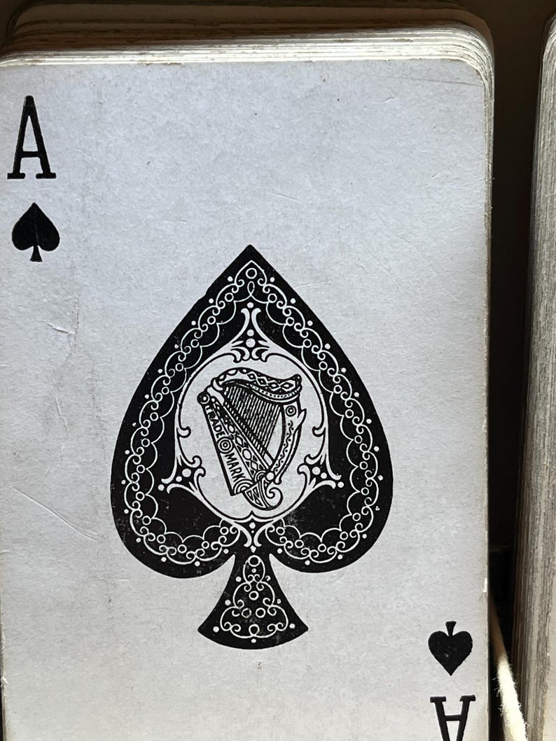 May include: Close-up of the Ace of Spades playing card. The card features a black spade symbol and the letter "A" in the upper left and lower right corners. The spade design includes a detailed harp illustration within a decorative border.