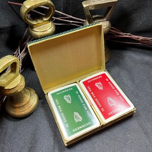 May include: A vintage gold-colored playing card box with two decks of cards. Each card has the Guinness logo and the text "IS GOOD FOR YOU". The box is open, revealing the green and red card backs.