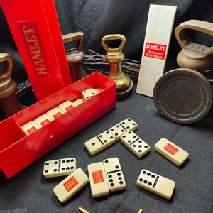 May include: A vintage domino set in a red box, with the word "HAMLET" printed on the box and dominoes. The dominoes are ivory-coloured with black dots. Red and yellow game pieces are also included.