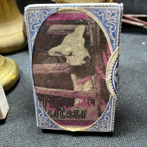 May include: Vintage matchbox with a blue and white decorative border. The central image features a cow behind a fence, with the word "Listers" and "THE NICEST WOOD" printed on the front.