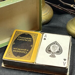 May include: A deck of playing cards in a box. The cards have a black and gold design with the words "Guinness is good for you" printed on them. One card shows the Ace of Spades.