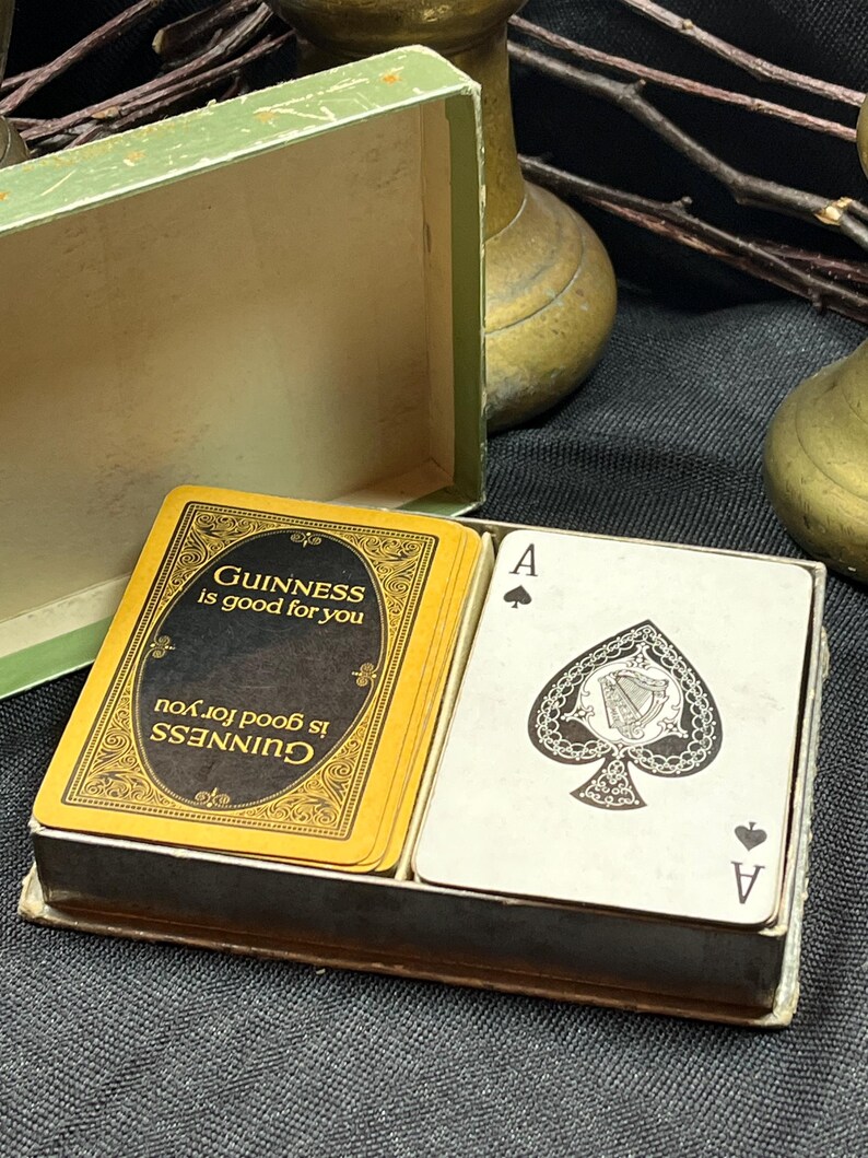 May include: A deck of playing cards in a box. The cards have a black and gold design with the words "Guinness is good for you" printed on them. One card shows the Ace of Spades.