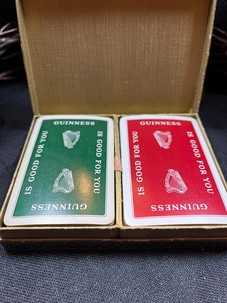 May include: A vintage Guinness playing card set in a gold-colored box. The cards are green and red, with the Guinness logo and the phrase "IS GOOD FOR YOU." Each card features a harp illustration.
