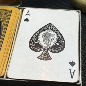 May include: Close-up of an Ace of Spades playing card. The card features a detailed black spade design with an ornate harp illustration in the center. The card is white with black accents and is part of a deck of cards.