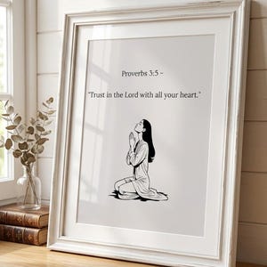 May include: A framed wall art print featuring a black and white line drawing of a person kneeling in prayer. The text above the illustration reads, "Proverbs 3:5 - Trust in the Lord with all your heart." The print is housed in a white wooden frame.