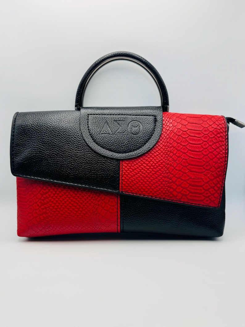 Pode incluir: Bolsa de m&atilde;o preta e vermelha com uma al&ccedil;a superior. A bolsa &eacute; dividida em duas se&ccedil;&otilde;es, com um lado preto e o outro vermelho com textura de pele de cobra. A aba superior apresenta as letras gregas Delta, Sigma e Theta.