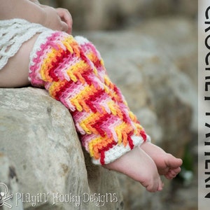 May include: A pair of colourful crochet leg warmers in shades of pink, orange, and yellow. The leg warmers are made with a textured stitch and have a white crocheted cuff. The leg warmers are worn by a child and are sitting on a rock.