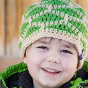 Peut inclure: Gros plan d'un jeune garçon portant un bonnet crocheté vert et crème. Le bonnet a un bouton sur le côté. Le garçon sourit.