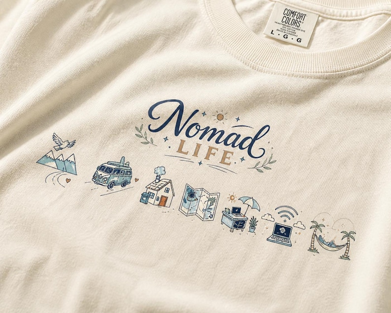 May include: Cream-colored t-shirt with the words "Nomad Life" in navy blue script. The design includes illustrations of a van, mountains, a house, a map, a laptop, and a hammock.