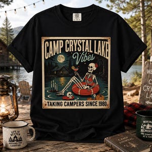 May include: Black t-shirt with a retro graphic of a skeleton in a lake, wearing an inner tube, and the words "Camp Crystal Lake Vibes." The design includes a full moon, cabin, and the text "Taking Campers Since 1980."