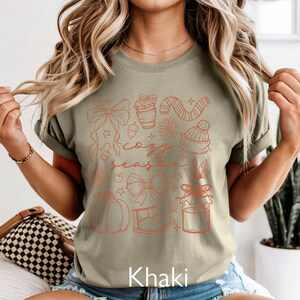 Peut inclure: T-shirt kaki avec un motif imprim&eacute; couleur rouille. Le motif comprend des n&oelig;uds, une tasse &agrave; caf&eacute;, une &eacute;charpe, un bonnet, une citrouille et l'inscription "cozy season".