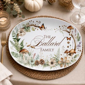Könnte beinhalten: Eine ovale weiße Servierplatte mit einer botanischen Illustration aus Farnen, Tannenzapfen, Pilzen und Schmetterlingen. Der Text "THE BALLARD FAMILY" ist mittig in dunkelbrauner Schrift gedruckt und von einem floralen Kranz umgeben.