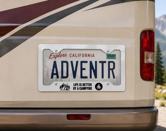 Op de afbeelding: Een zilverkleurig metalen kentekenplaathouder met de zwarte tekst 'LIFE IS BETTER BY A CAMPFIRE' en een afbeelding van een tent en kampvuur. De houder is bevestigd op een Californische kentekenplaat met de tekst 'ADVENTR' en 'Explore CALIFORNIA'.