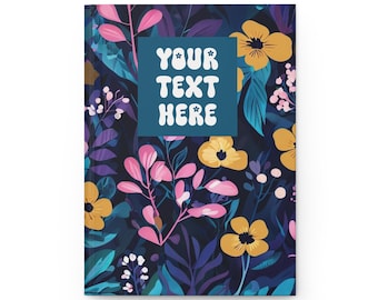 May include: A hardcover notebook with a floral design. The cover features a dark background with yellow, pink, and blue flowers and foliage. A blue square with the text "YOUR TEXT HERE" is centered on the cover.