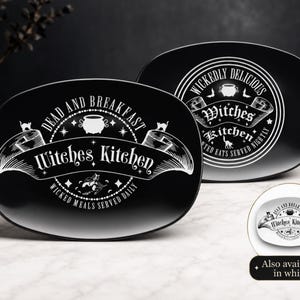 May include: Two oval black plates featuring white graphic designs. The front plate displays the text "DEAD AND BREAKFAST" and "Witches Kitchen" with a cauldron and cat illustration. The back plate features "WICKEDLY DELICIOUS" and "Witches Kitchen" text. A small white plate is shown as an option.