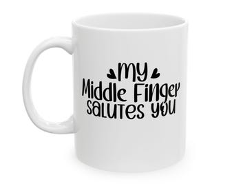 Könnte beinhalten: Weißer Keramikbecher mit gebogenem Henkel. Der Becher hat einen schwarzen Text, der "my Middle Finger salutes you" in einer verspielten Schriftart lautet. Der Becher hat eine Standardgröße und -form.