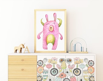 May include: A framed watercolor print of a pink monster with green horns and belly. The artwork is displayed on a white cabinet with floral design. Wooden unicorn and letter A are on the cabinet.