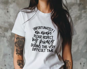 May include: White t-shirt with black text that reads "Unfortunately I am awake. Please respect my privacy during this very difficult time."