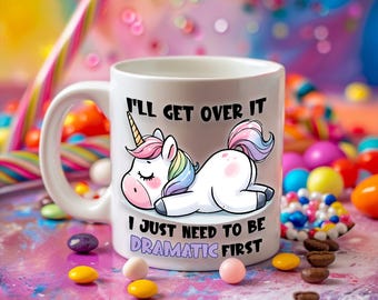 May include: White ceramic coffee mug with a cartoon unicorn lying down and the text "I'll get over it I just need to be dramatic first".