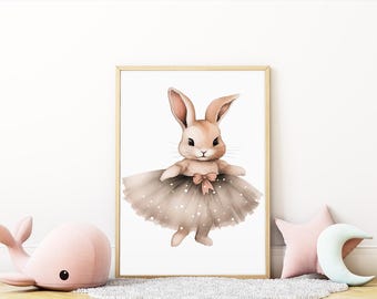 May include: Watercolor illustration of a bunny wearing a tutu. The bunny is light brown with long ears and a pink bow. The tutu is a light brown with white polka dots. The framed artwork is displayed with a pink whale and star-shaped pillow.