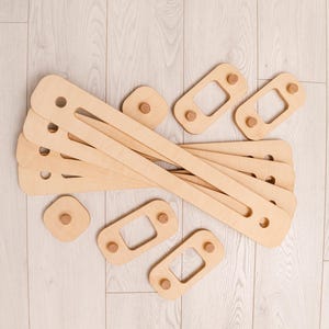 May include: A selection of unfinished wooden toy components. There are long, rectangular pieces with holes, alongside smaller square and rectangular pieces with wooden pegs. The light brown pieces are likely for a construction toy.