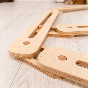 May include: A natural wood climbing frame, with a light-coloured finish. The frame is made from multiple rectangular and rounded wooden pieces, joined with wooden dowels. The design suggests a focus on children's play and development.