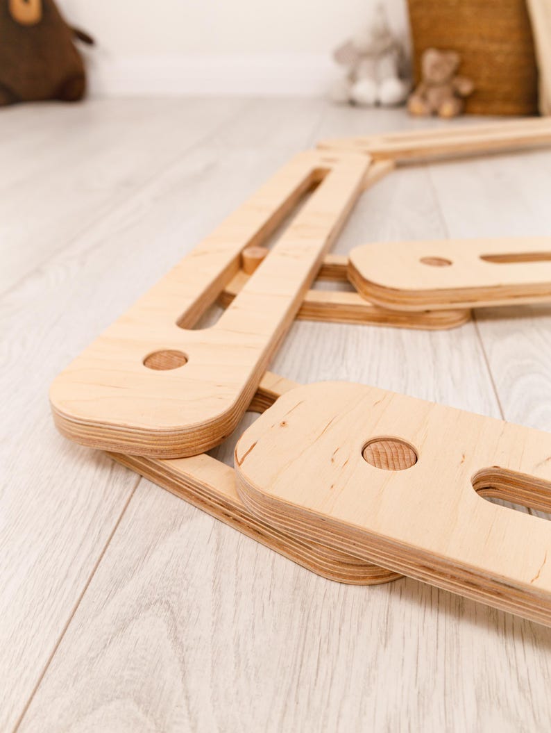 May include: A natural wood climbing frame, with a light-coloured finish. The frame is made from multiple rectangular and rounded wooden pieces, joined with wooden dowels. The design suggests a focus on children's play and development.