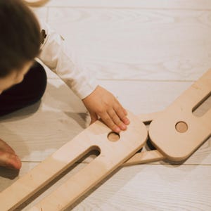 May include: Wooden toy set with interlocking pieces and a circular wooden piece. The natural wood colour is visible. The toy is designed for children's play and development.