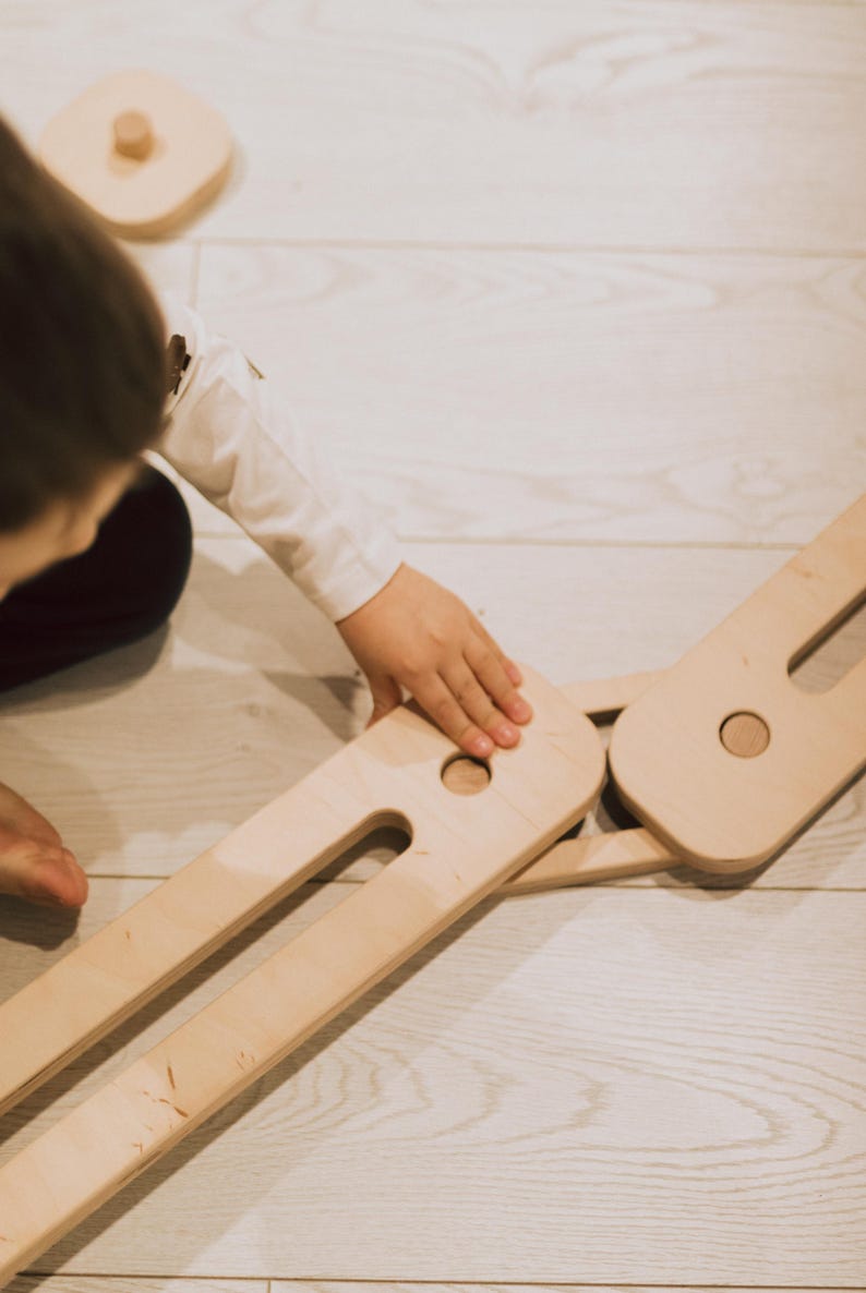 May include: Wooden toy set with interlocking pieces and a circular wooden piece. The natural wood colour is visible. The toy is designed for children's play and development.