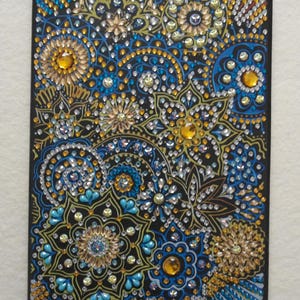 May include: A black canvas with a colourful diamond painting of blue, yellow, and white floral patterns. The design features intricate swirls and flowers.