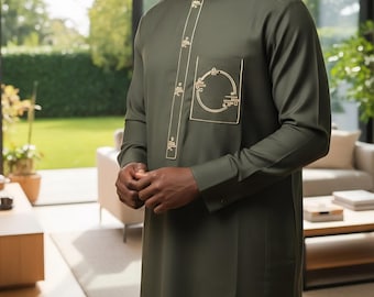 May include: Olive green tunic with long sleeves and a mandarin collar. The tunic features gold-colored embroidered detailing on the front and a pocket. The outfit is worn by a person in a well-lit room with a view of a green lawn.