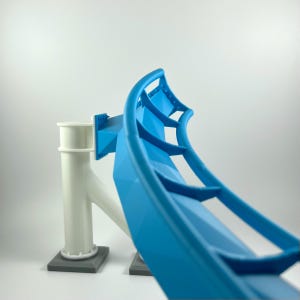 Puede incluir: Un modelo de vía de montaña rusa impreso en 3D azul y blanco. La vía es curva y tiene una estructura de soporte.