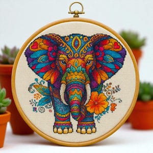 Peut inclure: Broderie au point de croix colorée d'un éléphant dans un cercle en bois. L'éléphant est orné de motifs complexes dans des tons de bleu, orange, violet et jaune. Des motifs floraux entourent l'éléphant, et le cercle a une boucle de suspension en métal.