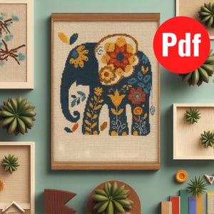 Peut inclure: Une broderie au point de croix encadrée représentant un éléphant bleu orné de motifs floraux colorés. L'éléphant est encadré dans un cadre en bois brun clair. L'image est entourée d'autres œuvres d'art encadrées et de succulentes décoratives.